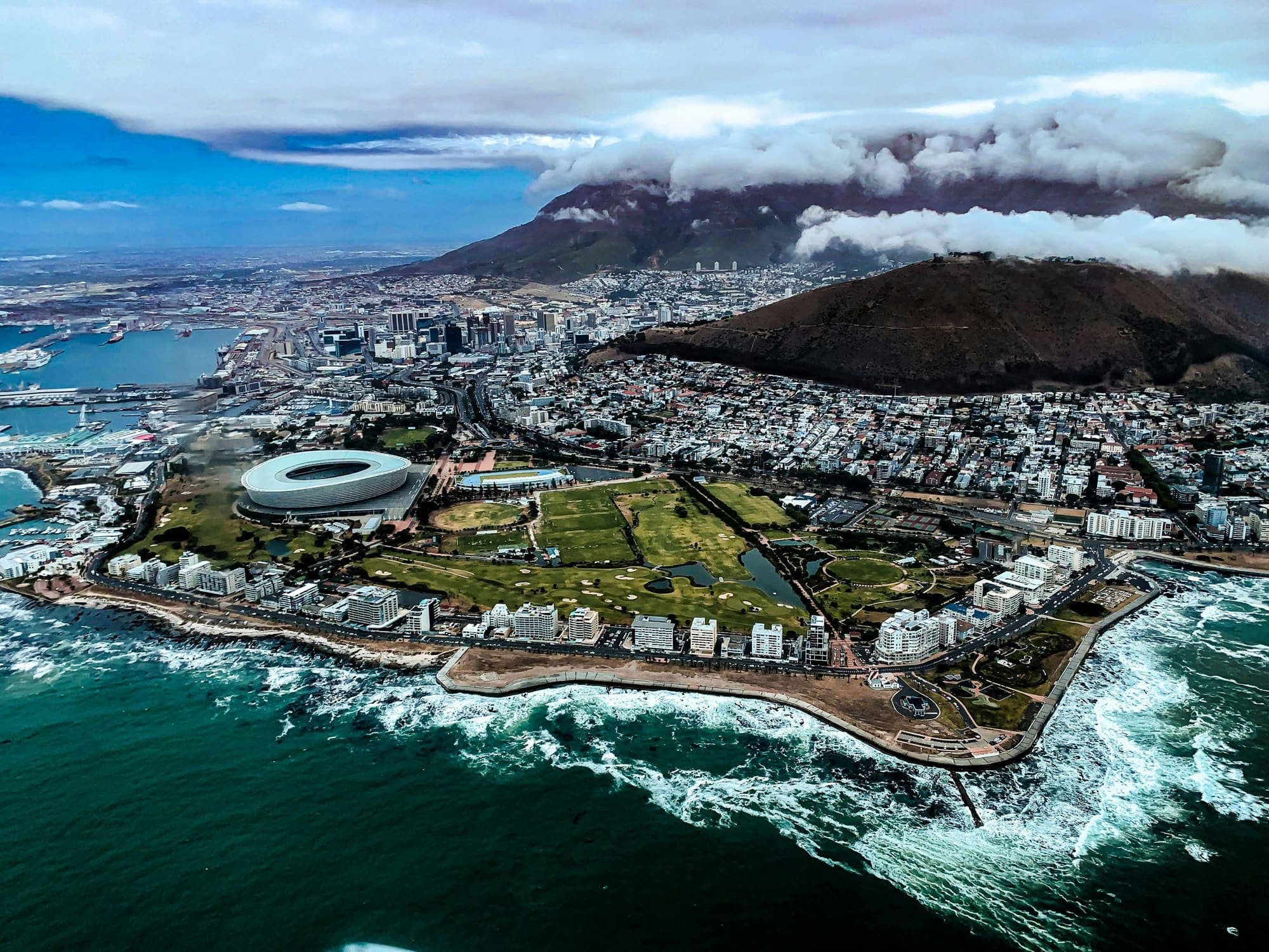 Aerial view of Green Point and the Atlantic coast beneath a tablecloth cloud pouring over Table Mountain